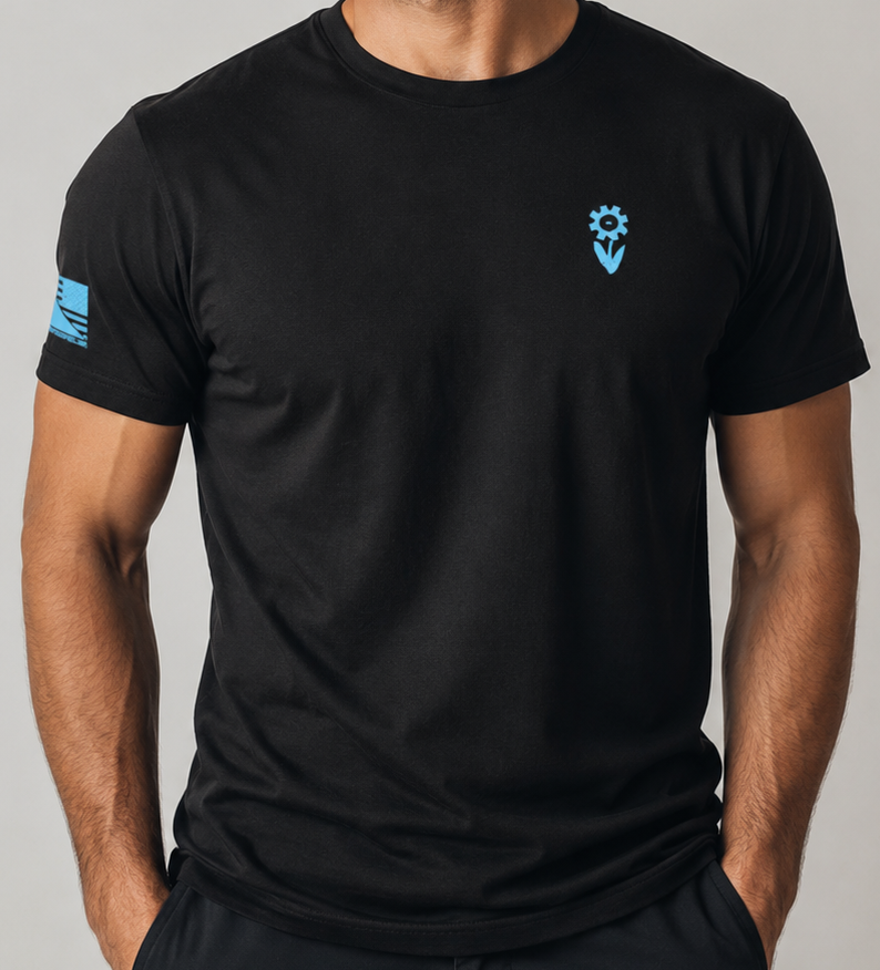 A man wearing a black short-sleeve crewneck t-shirt with a small light blue logo on the left chest and a light blue graphic on the right sleeve, photographed against a neutral gray studio background.