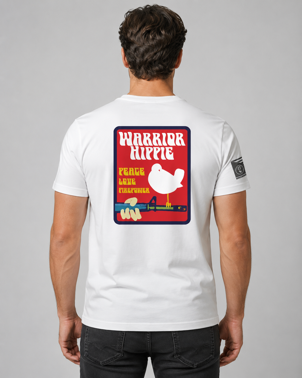 A man viewed from behind wearing a white t-shirt with a large red, yellow, and blue graphic on the back that reads 'WARRIOR HIPPIE PEACE AND LOVE' with a white bird illustration, and a small black square patch on the left sleeve.
