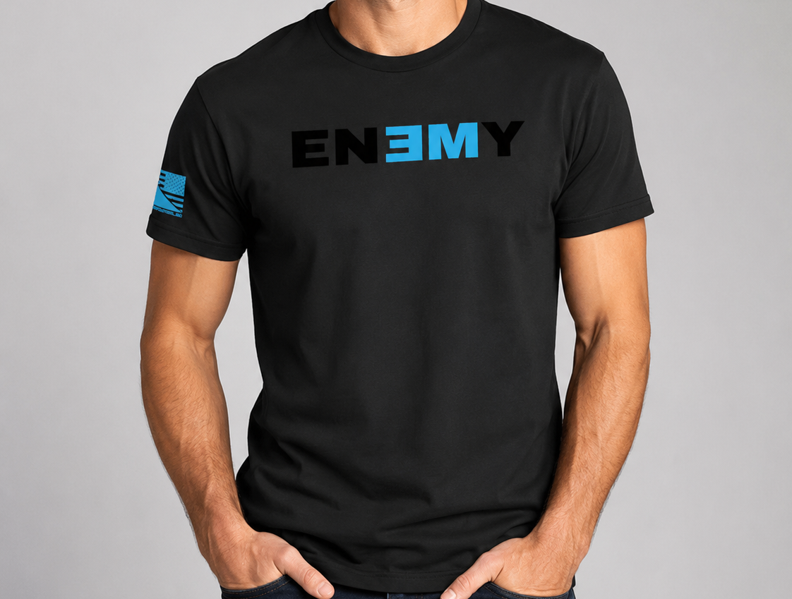 A man wearing a black short-sleeve t-shirt with a graphic print on the chest and sleeve. The graphic features the word 'ENEMY' in black and bright blue letters, with a matching blue flag design on the right sleeve.